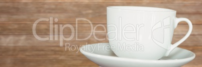 White cup with saucer against blurry wood panel