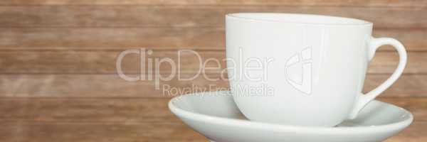 White cup with saucer against blurry wood panel