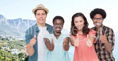 Group of friends giving thumbs up against blurry coastline