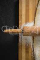 Cropped image of rolling pin on dough over cutting board