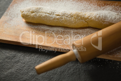 Raw bread with flour and rolling pin on cutting board