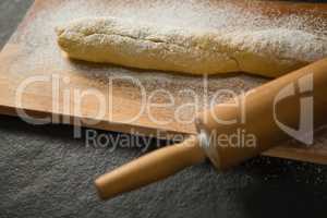 Raw bread with flour and rolling pin on cutting board
