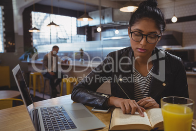 Woman with laptop reading book in cafe