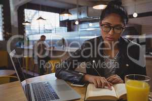 Woman with laptop reading book in cafe