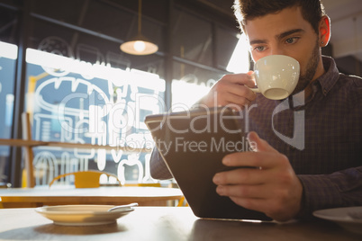 Man drinking coffee while using tablet in cafe