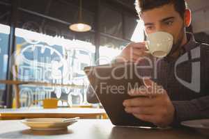 Man drinking coffee while using tablet in cafe