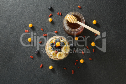 Honey dipper with cup of yogurt muesli, banana and blueberries for breakfast