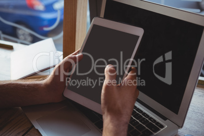 Cropped hands holding tablet by laptop in cafe