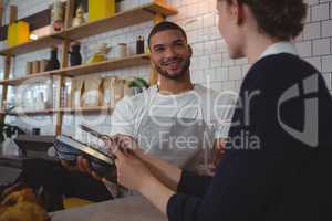 Young waiter showing credit card reader to owner in cafe