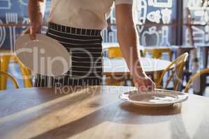 Mid section of waiter arranging plates on table