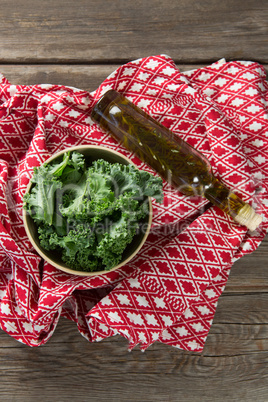 Fresh kale leaves with oil bottle and fabric on table