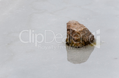 Single rock reflected in melting ice.