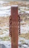 Rusted square metal post with two hanging chains.