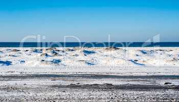 Frozen dunes on beach against water and sky.