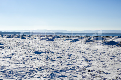 Frozen ice, snow, and sand dunes on beach with hills in distance