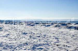 Frozen ice, snow, and sand dunes on beach with hills in distance
