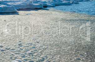 Melting ice chunks by water and frozen shore.