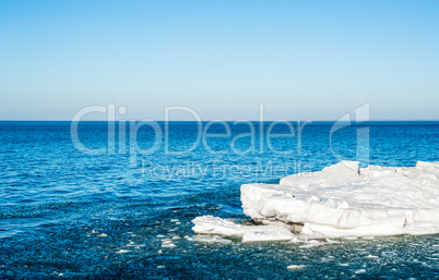 Melting ice chunks floating into blue water under empty sky.