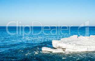 Melting ice chunks floating into blue water under empty sky.