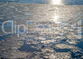 Melting ice sheet on water reflecting sunlight.