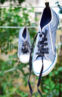 old blue sneaker hanging on a rope behind a wooden clothespin
