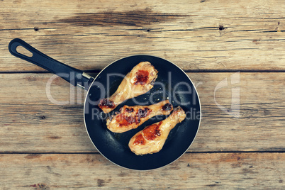 Chicken grilled legs. Fried chicken legs in a frying pan on a wooden table