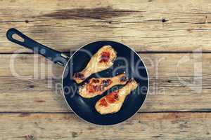 Chicken grilled legs. Fried chicken legs in a frying pan on a wooden table