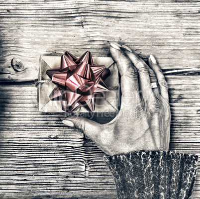 Closeup of a smartphone in the hands of a woman and a gift box with a red bow on a wooden table.
