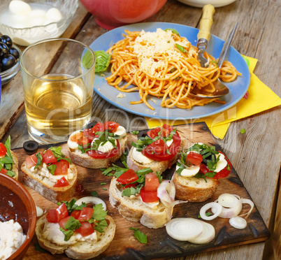 Varied snacks on the dining table, wine, pasta and bruschettes with avocado and cherry tomatoes closeup.