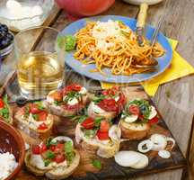 Varied snacks on the dining table, wine, pasta and bruschettes with avocado and cherry tomatoes closeup.