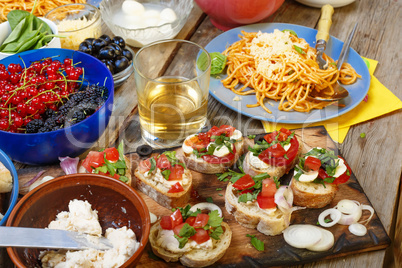Varied snacks on the dining table, wine, pasta and bruschettes with avocado and cherry tomatoes closeup.