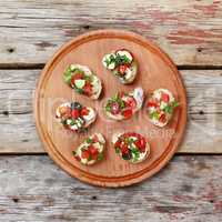 Delicious Italian bruschetta with roasted tomatoes, mozzarella cheese and herbs on a cutting board