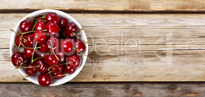 Ripe Cherry  In a white bowl on a wooden background, rural style. View from above