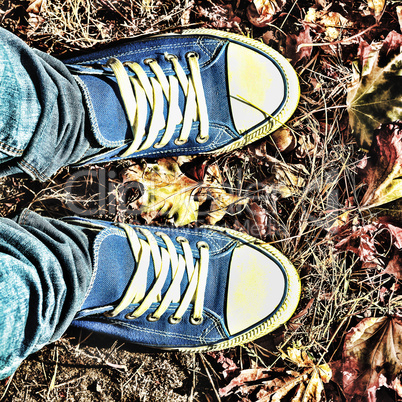 Autumn background. Legs of a young woman in a blue sneakers
