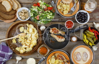 Outdoors Food Concept. Appetizing barbecued chicken legs, chips and a salad of fresh vegetables on a wooden picnic table, top view