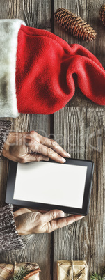 Tablet computer in the human hands. Near the table with tablet computer gift boxes, christmas bell and fluffy fir branches. Free space for text. top view. Copy space.