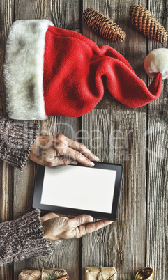 Tablet computer in the human hands. Near the table with tablet computer gift boxes, christmas bell and fluffy fir branches. Free space for text. top view. Copy space.