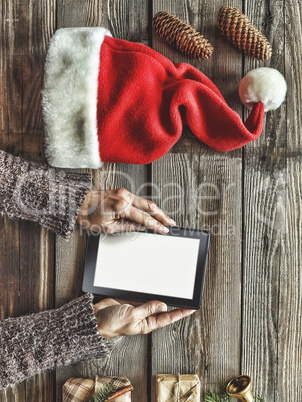 Tablet computer in the human hands. Near the table with tablet computer gift boxes, christmas bell and fluffy fir branches. Free space for text. top view. Copy space.