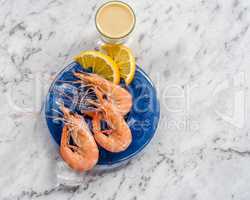 Shrimp on blue plate with sauce white marble background.