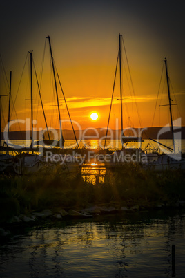 Silhouette of sailing boats on a calm lake at sunset.