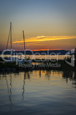 Silhouette of sailing boats on a calm lake at sunset.