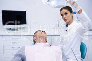 Dentist adjusting electric light while patient sitting on dental chair
