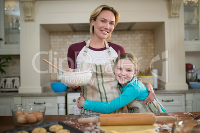 Daughter hugging mother while preparing cookies in kitchen