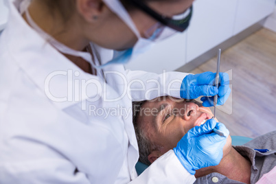 Dentist holding tools while examining man at clinic