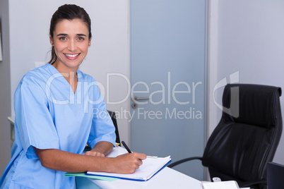 Portrait of doctor writing in file while sitting by table