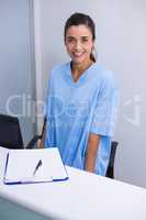 Portrait of smiling doctor standing at desk against wall