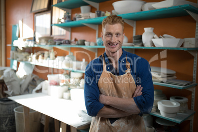 Male potter standing with arms crossed in pottery workshop