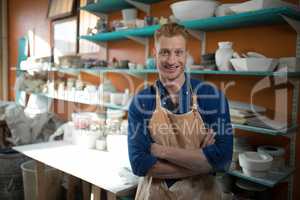 Male potter standing with arms crossed in pottery workshop