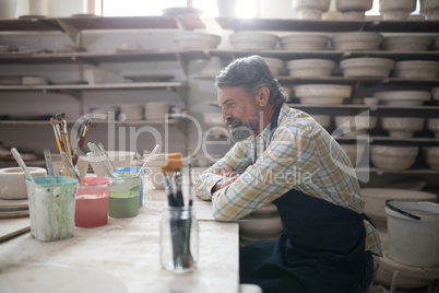 Thoughtful male potter sitting at worktop