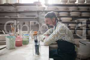 Thoughtful male potter sitting at worktop